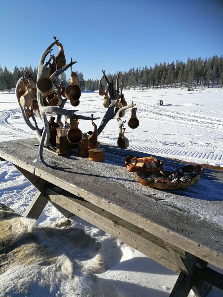 Rustikaler Holztisch mit klassischen Sami Holztassen und Fellen für die Pause beim Eisangeln.
